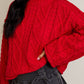 Person wearing a red cable knit sweater with a neutral background