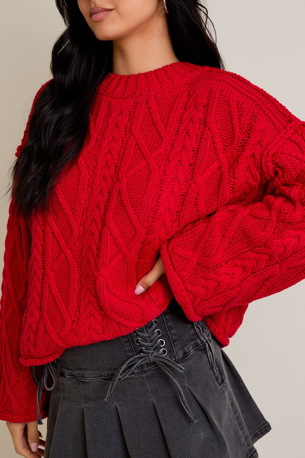Person wearing a red cable knit sweater with a neutral background