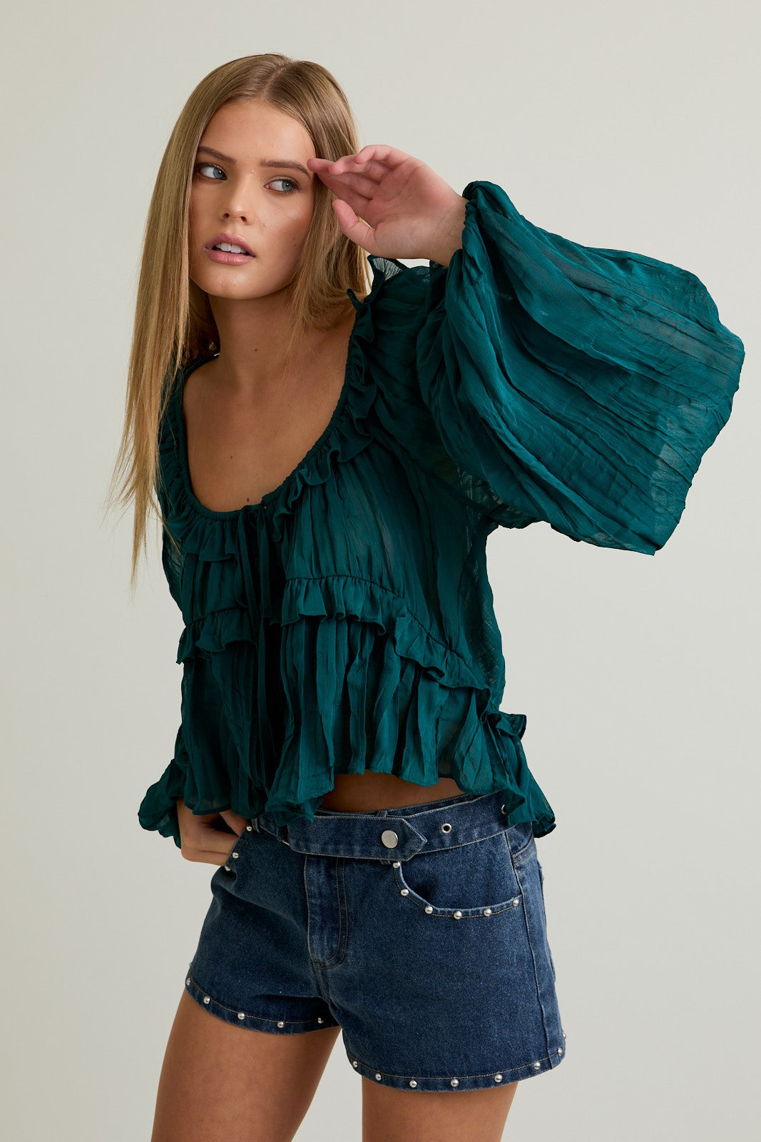 Woman wearing a green ruffled blouse and denim shorts on a plain background