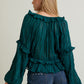 Woman wearing a teal blouse with ruffled details and denim shorts on a plain background