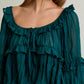 Teal ruffled blouse worn by a person on a neutral background