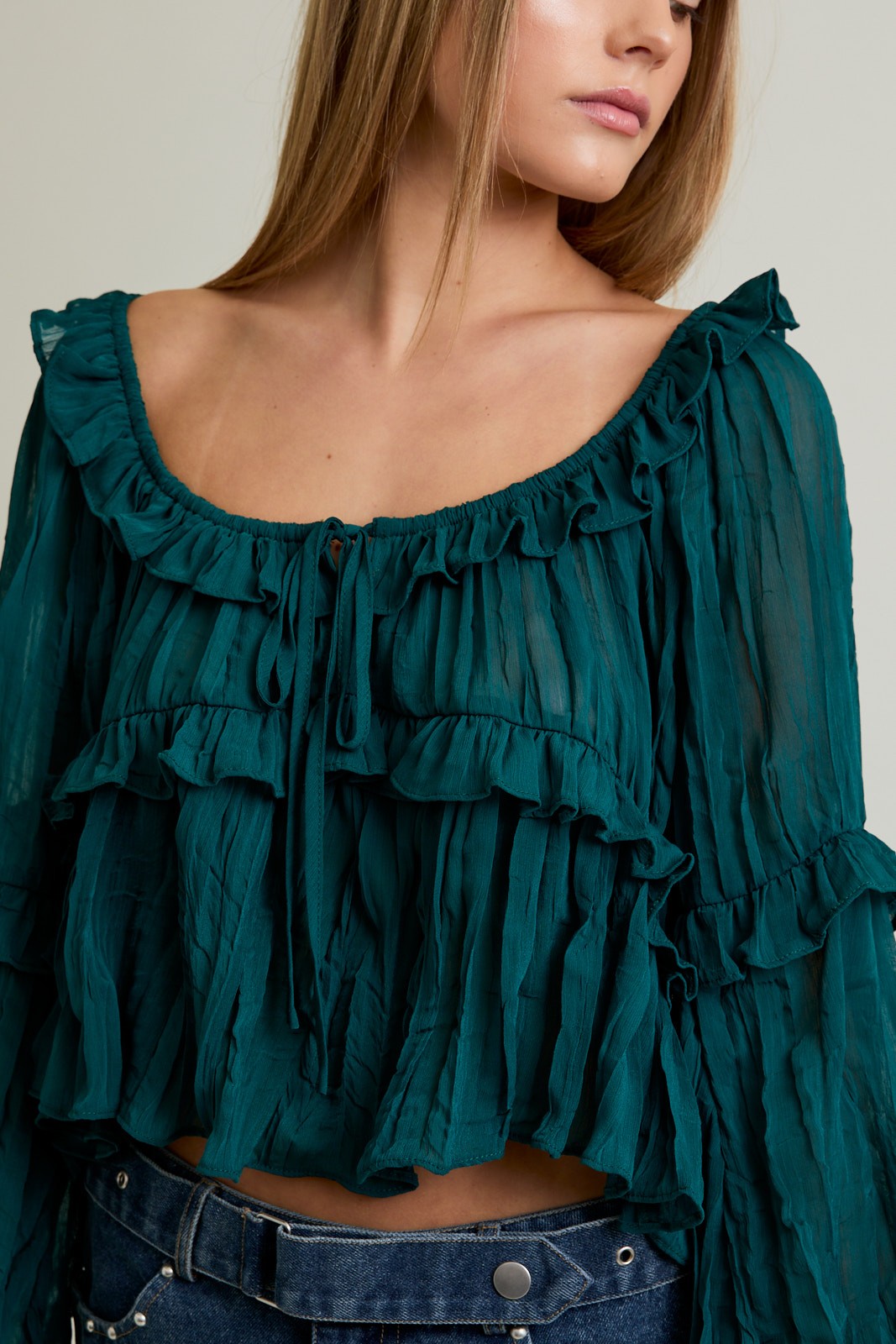 Teal ruffled blouse worn by a person on a neutral background