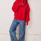 Person wearing a red sweatshirt and blue patterned pants against a white wall.