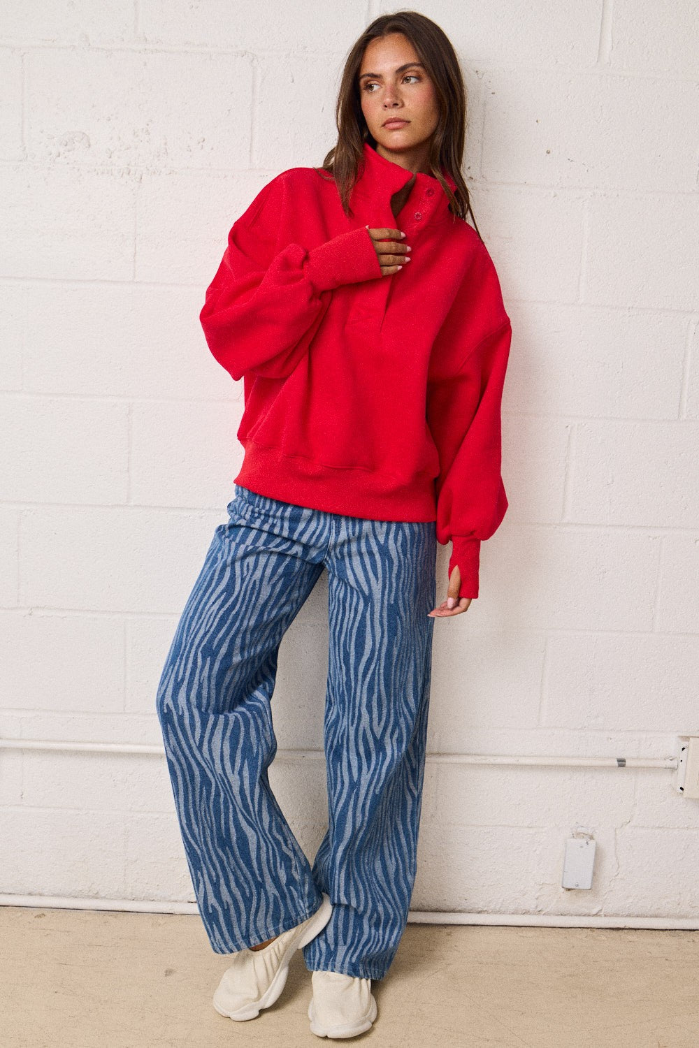 Person wearing a red sweatshirt and blue patterned pants against a white wall.