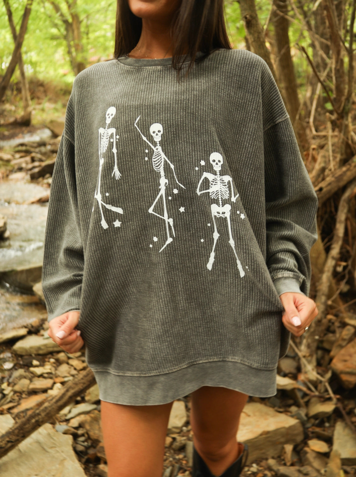 Person wearing a gray sweatshirt with skeleton designs in a forest setting