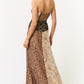Back view of a woman in a patchwork-style maxi dress with spaghetti straps, leopard and tie-dye panels, and a flowing hem.