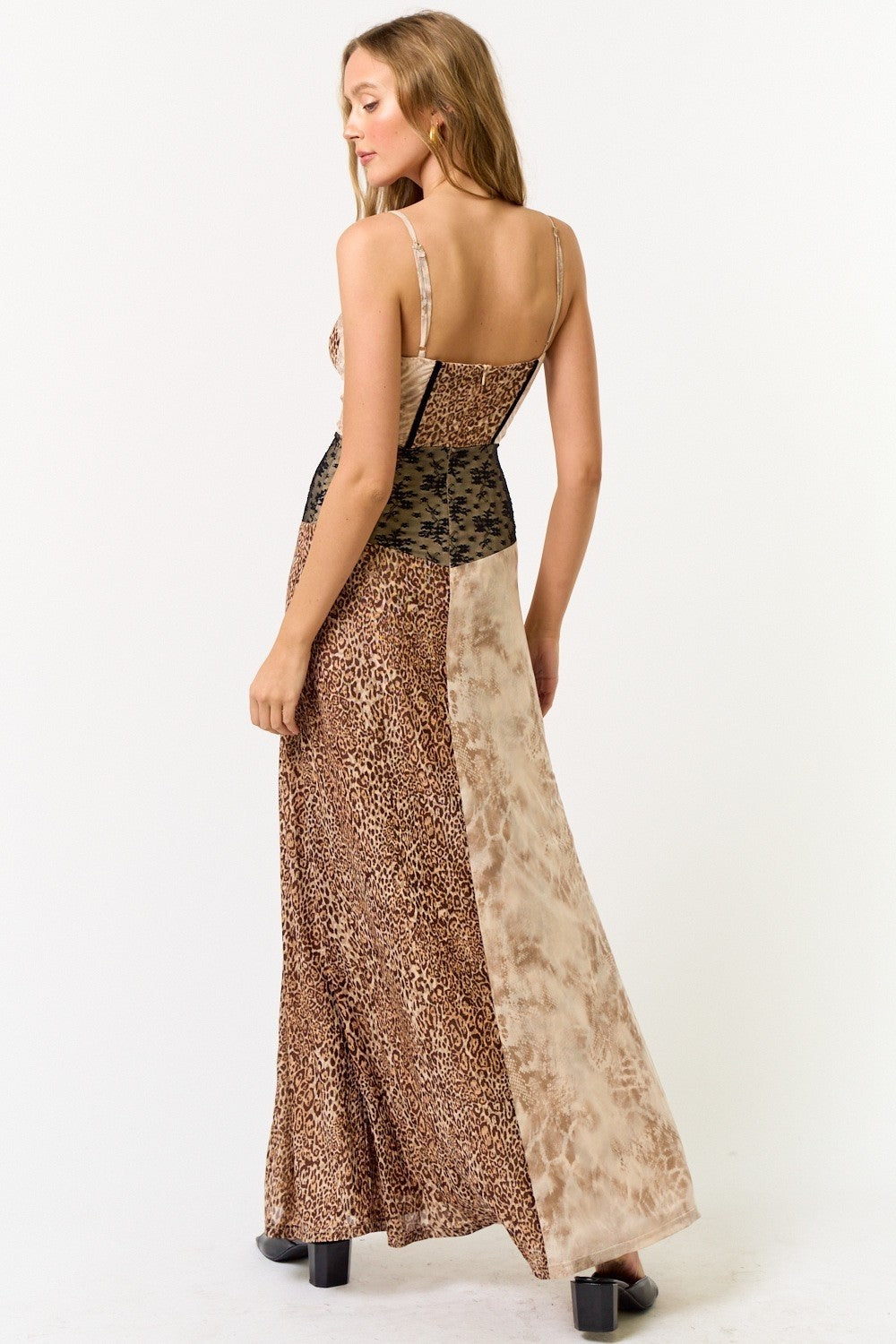 Back view of a woman in a patchwork-style maxi dress with spaghetti straps, leopard and tie-dye panels, and a flowing hem.