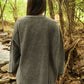 Person wearing a gray oversized sweater in a forest setting