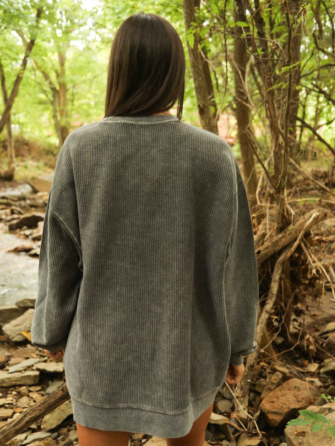 Person wearing a gray oversized sweater in a forest setting