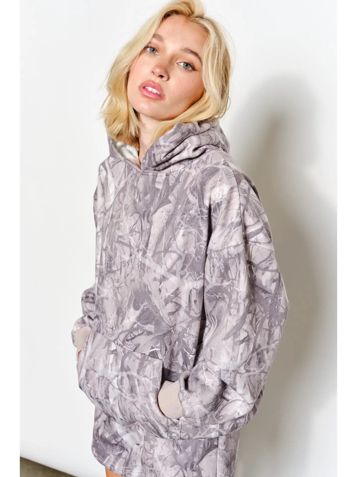 Person wearing a gray camouflage hoodie against a white background
