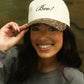 Woman wearing a cap with 'Boo!' text, smiling outdoors.