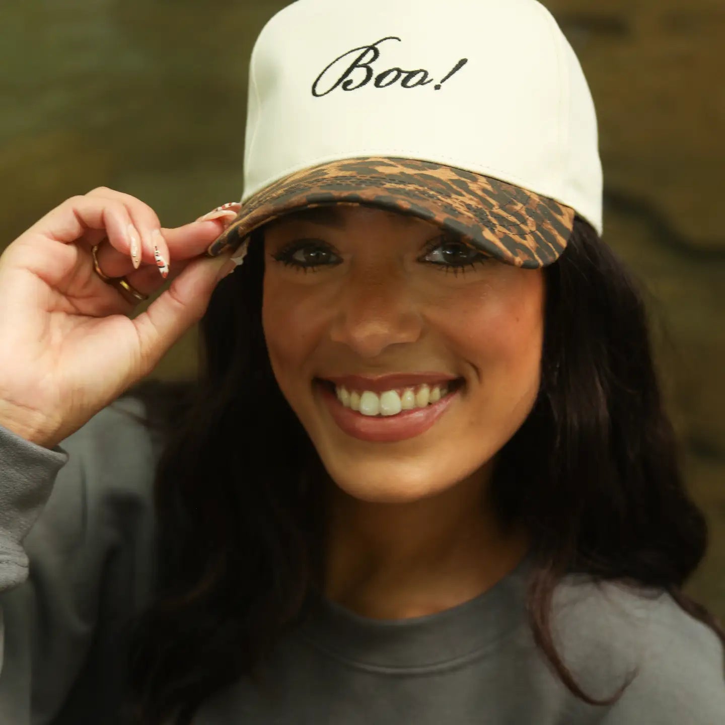 Woman wearing a cap with 'Boo!' text, smiling outdoors.