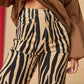 Person wearing zebra print pants with a brown coat against a beige background