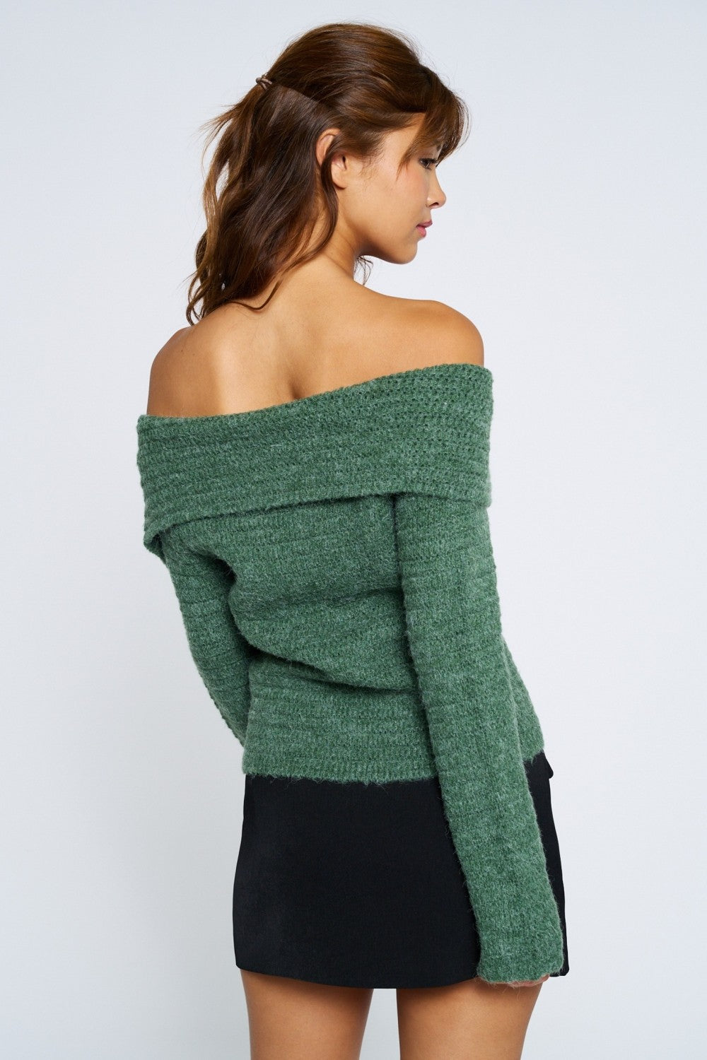 Woman wearing a green off-shoulder sweater and black skirt on a white background