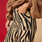 Person wearing a brown coat and zebra-striped pants against a red background