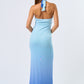 Back of Woman wearing a blue ombré halter maxi dress with front cutout, standing against a plain white background.