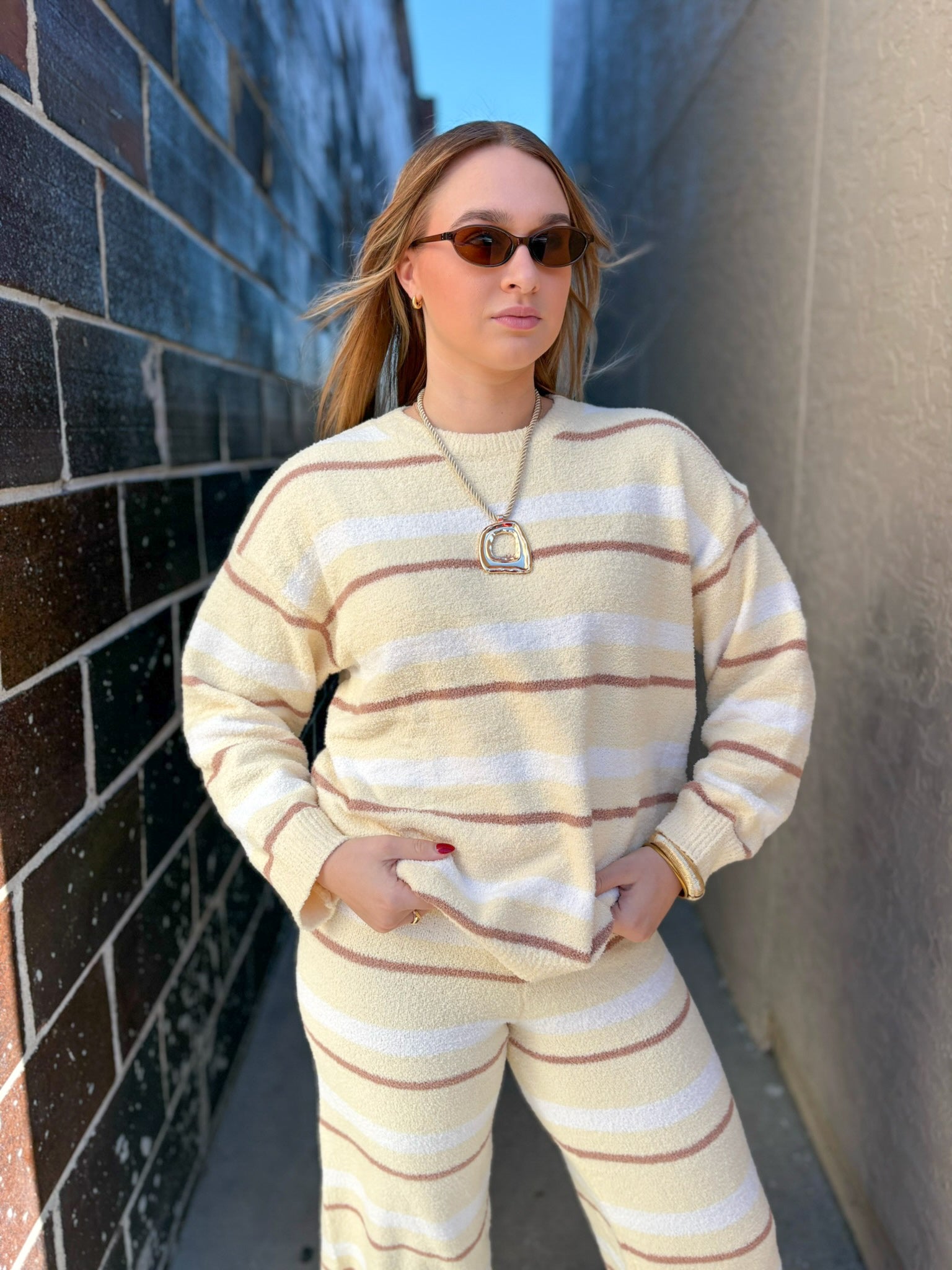 Woman wearing a beige and white striped sweater and pants against a brick wall.