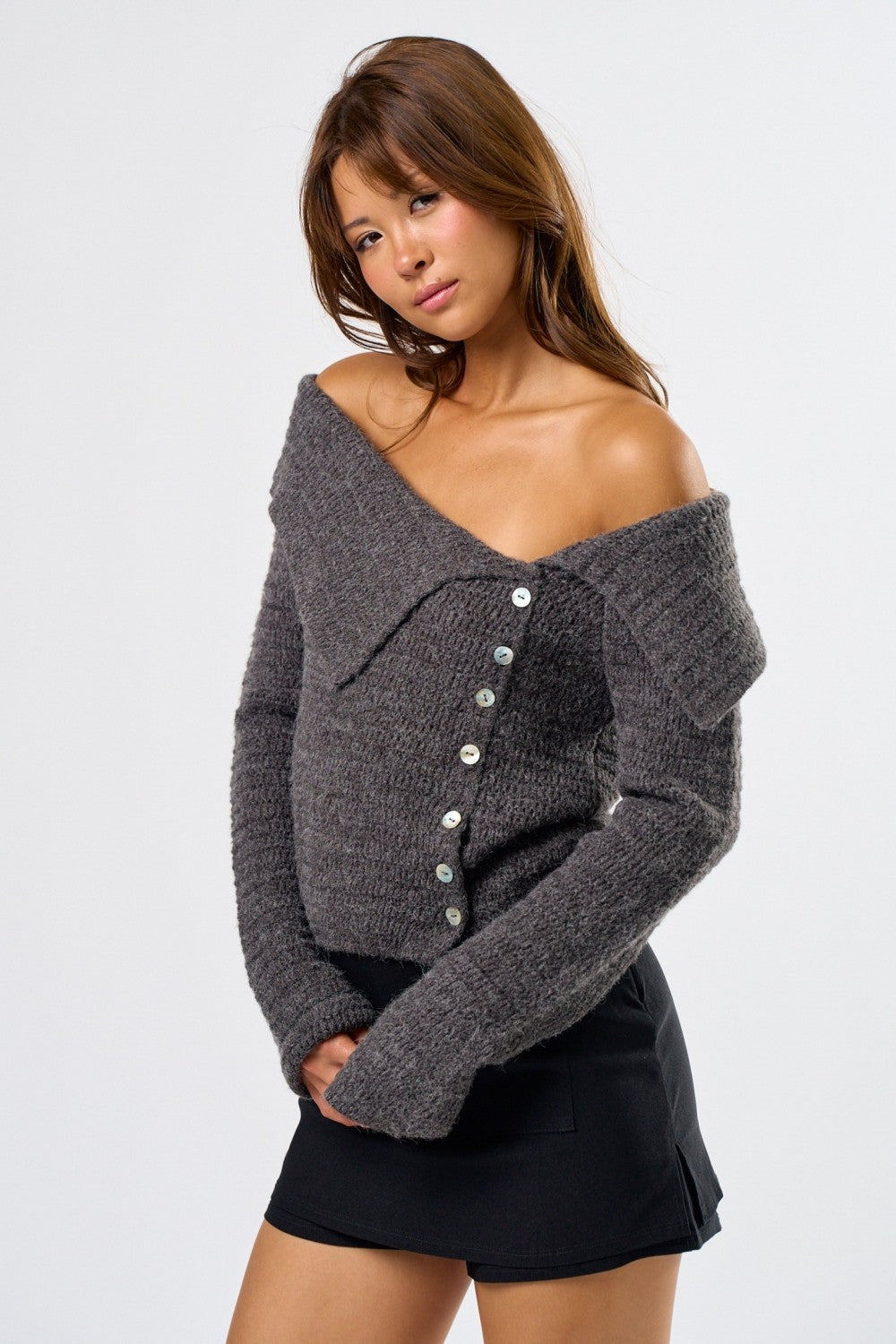 Woman wearing a gray off-shoulder sweater with buttons on a white background