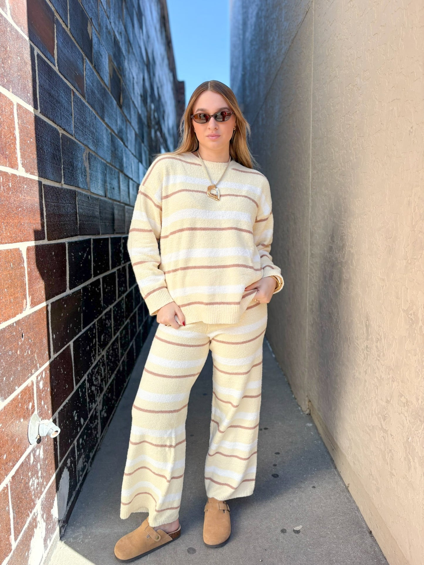 Person wearing a matching striped sweater and pants set standing against a textured wall.