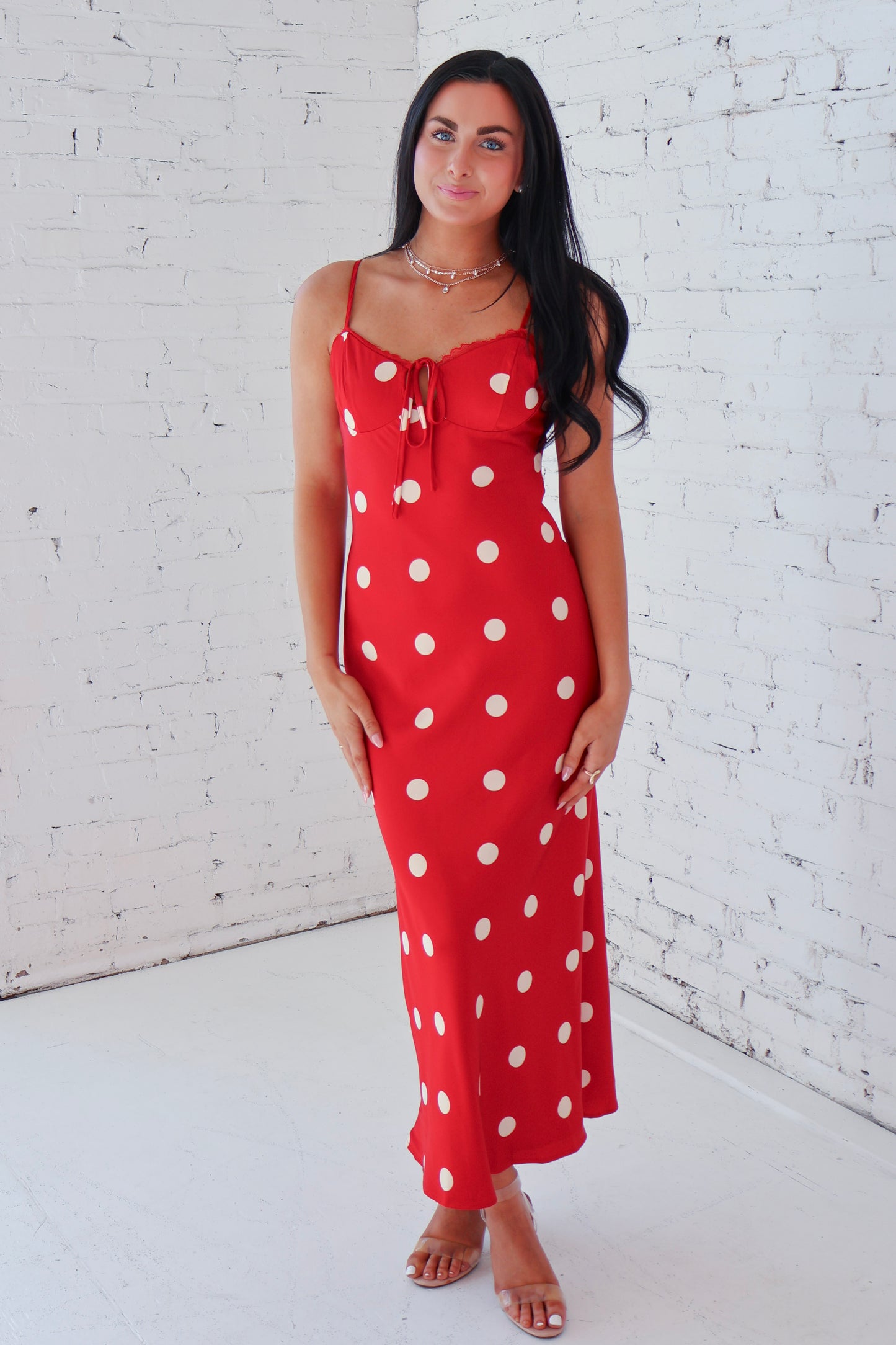Woman wearing a red dress with white polka dots against a white brick wall.
