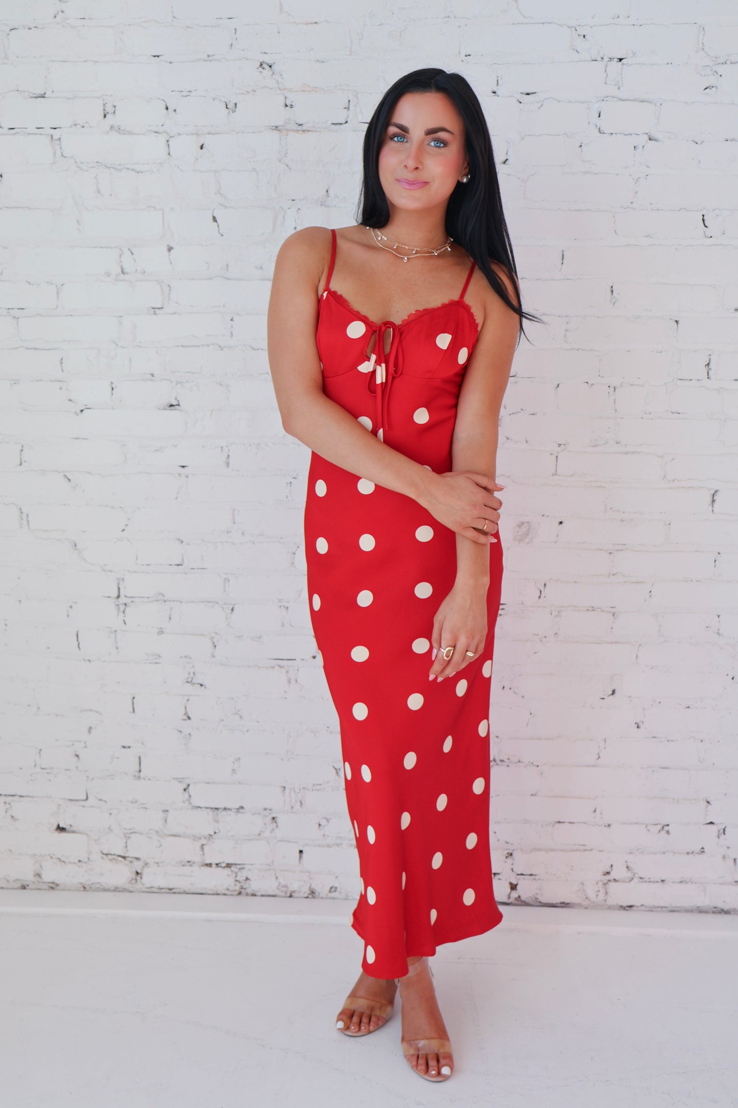 Woman wearing a red polka dot dress against a white brick wall.