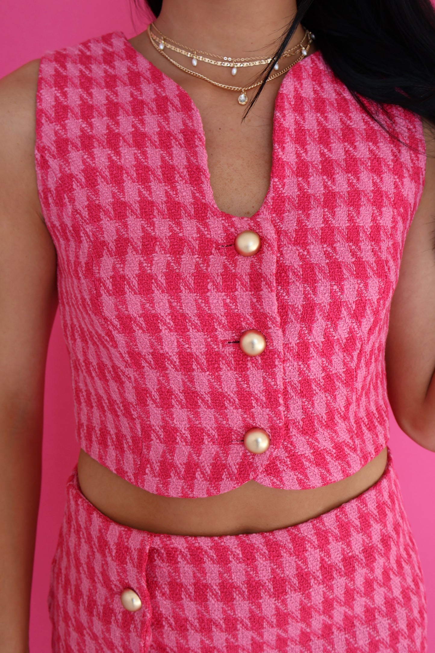 Person wearing a pink houndstooth patterned outfit with buttons on a pink background