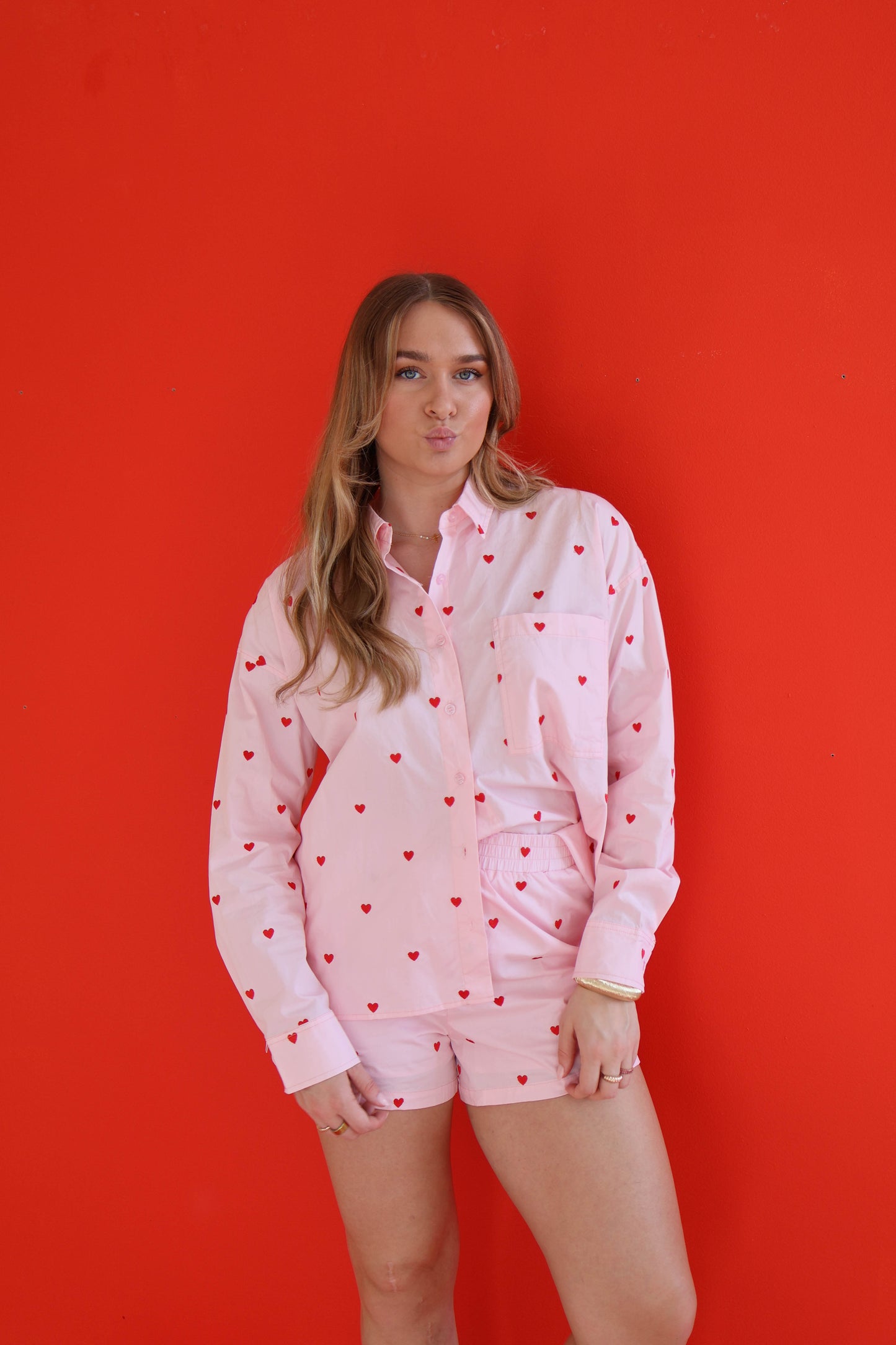 Woman wearing a pink shirt with heart patterns and shorts against a red background