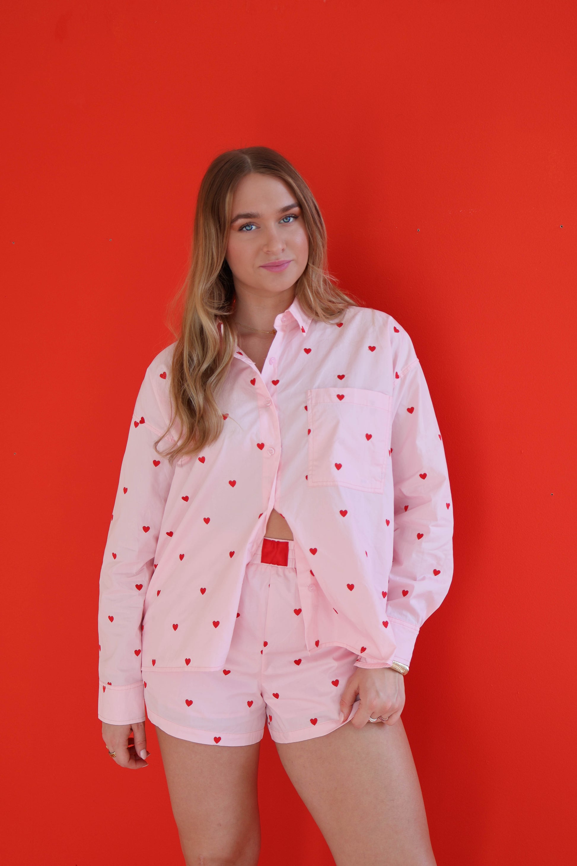 Woman wearing a pink outfit with heart patterns against a red background
