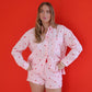 Woman wearing a pink shirt with heart patterns and shorts against a red background