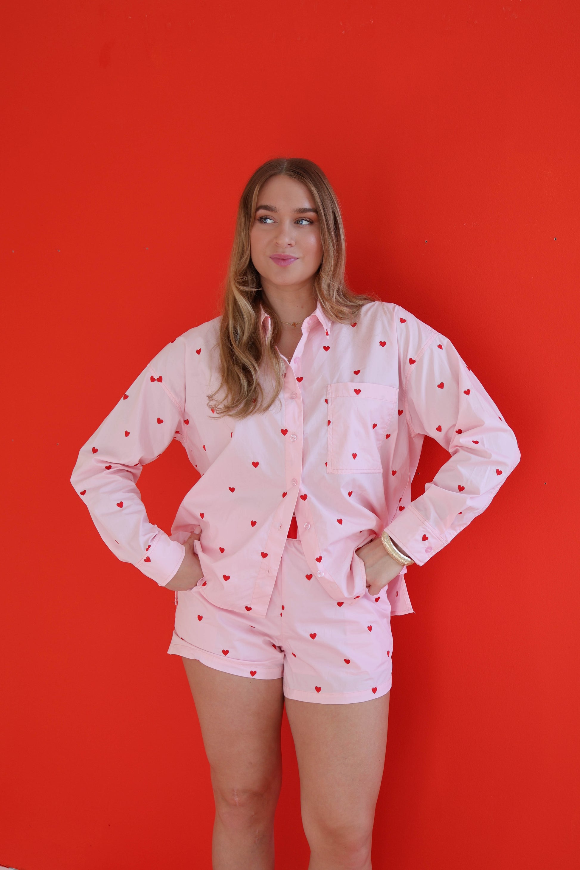 Woman wearing a pink shirt with heart patterns and shorts against a red background
