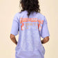 Vintage-inspired Fleetwood Mac Rumours Tour T-shirt in a soft, faded lavender wash, featuring a retro band logo and star graphic on the front. The back showcases 1977-1978 tour dates and locations, with bold lettering and a nostalgic rock aesthetic. Designed in an oversized, relaxed fit, this tee is perfect for music lovers and casual streetwear styling.