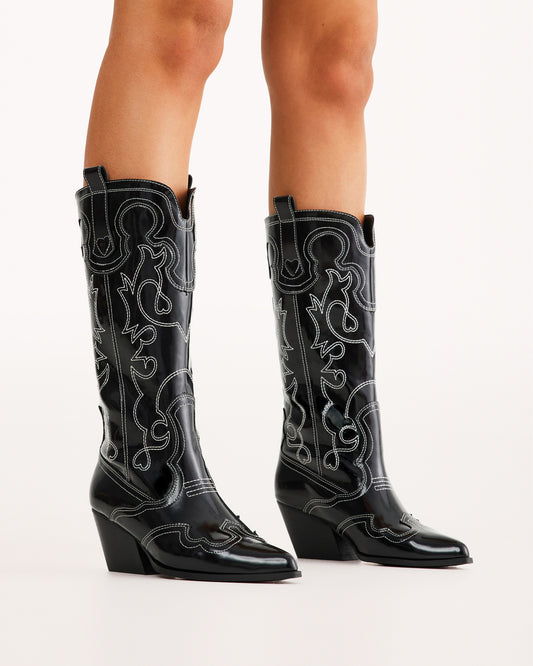 Sleek and bold, these black patent western boots feature contrasting white stitching, a pointed toe, and a stacked angled heel for a modern twist on classic cowboy style. Perfect for concerts, festivals, and statement outfits.