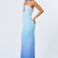 side view Woman wearing a blue ombré halter maxi dress with front cutout, standing against a plain white background.
