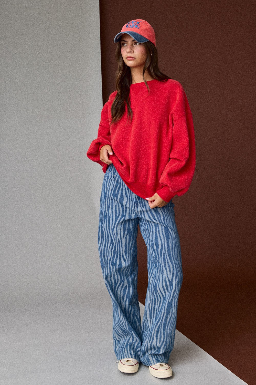Person wearing a red sweater and blue patterned pants against a gradient wall.