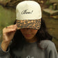 Person wearing a cap with 'Boo!' text and leopard print brim, outdoors.
