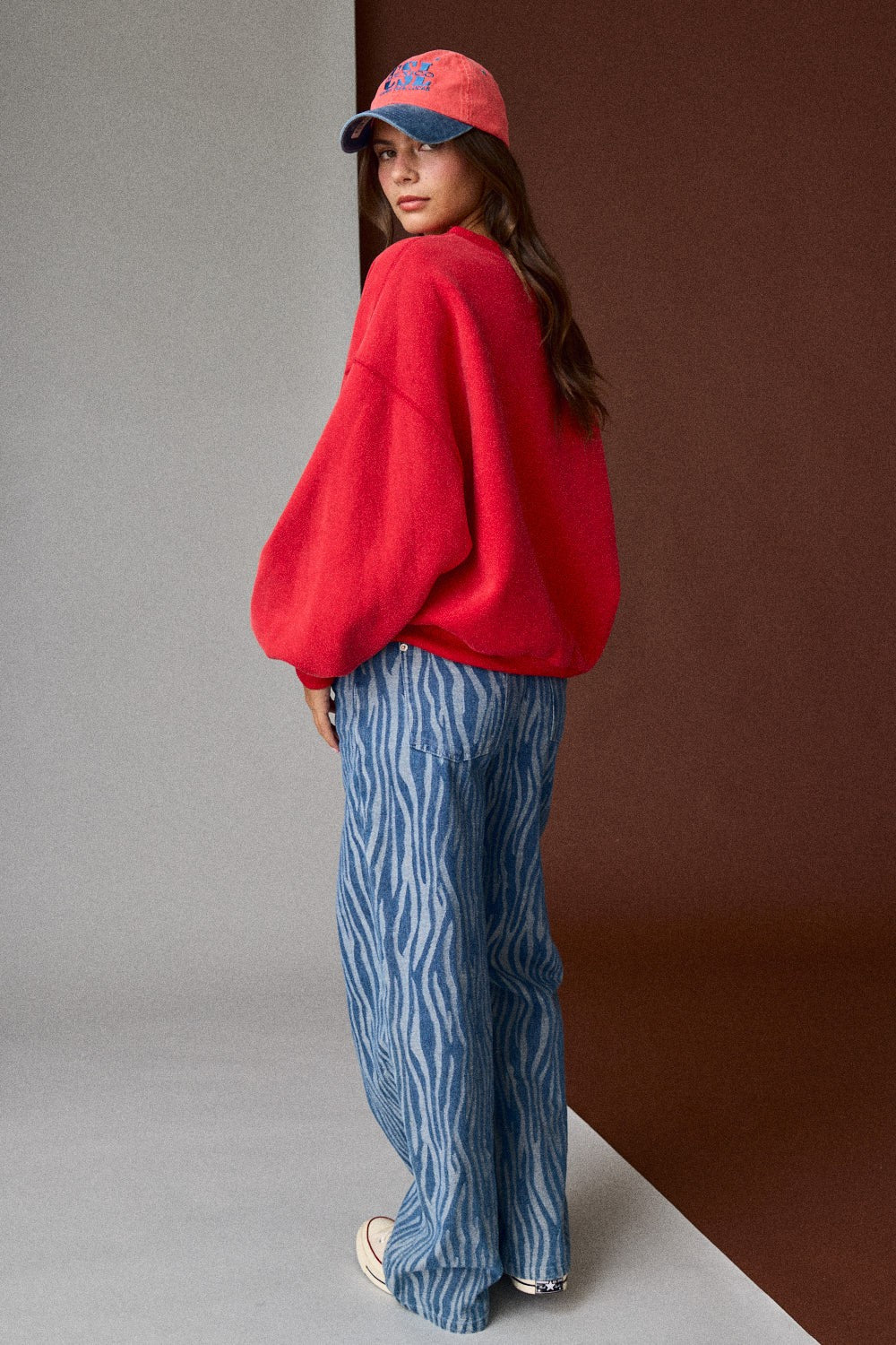 Person wearing a red sweater and blue patterned pants against a gradient wall.
