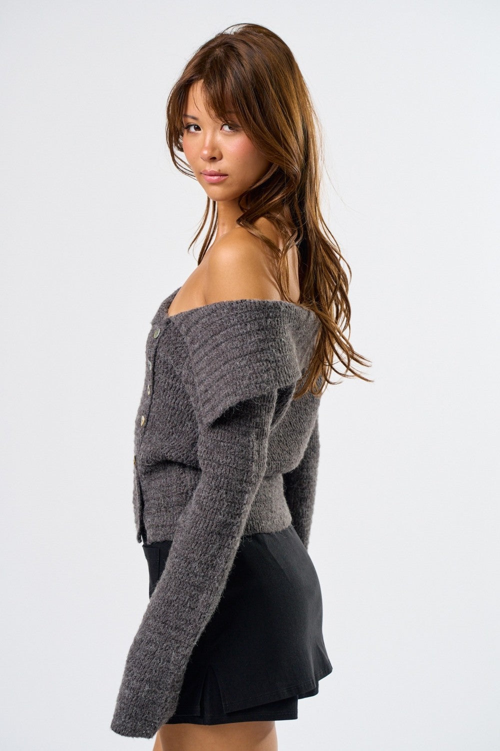 Woman wearing a gray off-shoulder sweater and black skirt on a white background