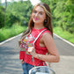 Woman posing confidently in a red Kansas City Chiefs sleeveless crop top, blue jeans with white side stripes, and holding a clear crossbody bag shaped like a football, standing on a road surrounded by trees.
